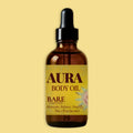 A 1 fl oz amber glass dropper bottle of Aura Body Oil, Bare Unscented, centered against a solid pale yellow background.