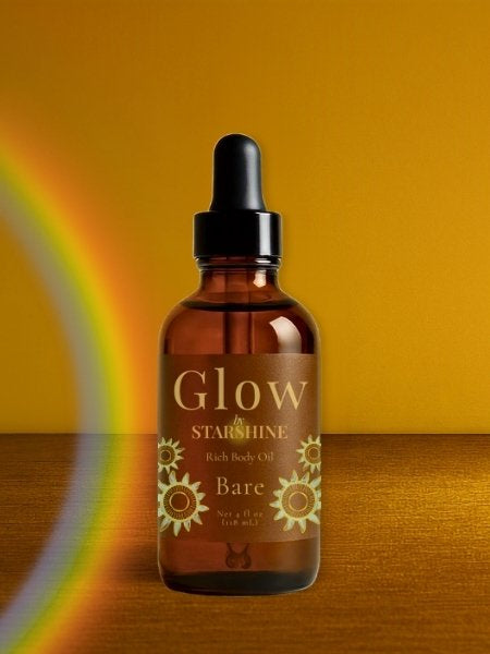 brown bottle of hair oil that says "glow" with a rainbow beside it and a brown background