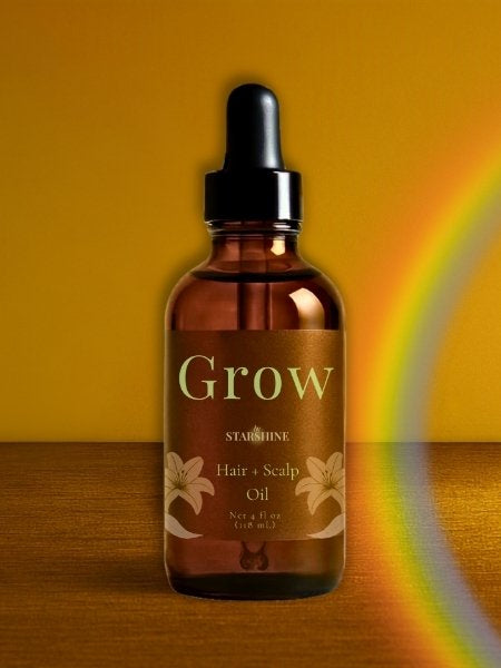 A bottle of bySTARSHINE Grow Hair + Scalp Oil in an amber glass dropper bottle with a black cap, set against a warm yellow background with a rainbow light effect on the right.