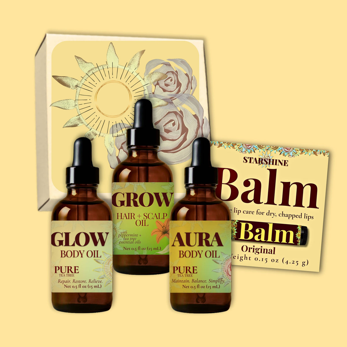 Three amber glass dropper bottles labeled Glow, Grow, and Aura tea tree scented body oil for dry skin with black caps are arranged in front of a white gift box with floral artwork, alongside a brown balm packet labeled Balm.
